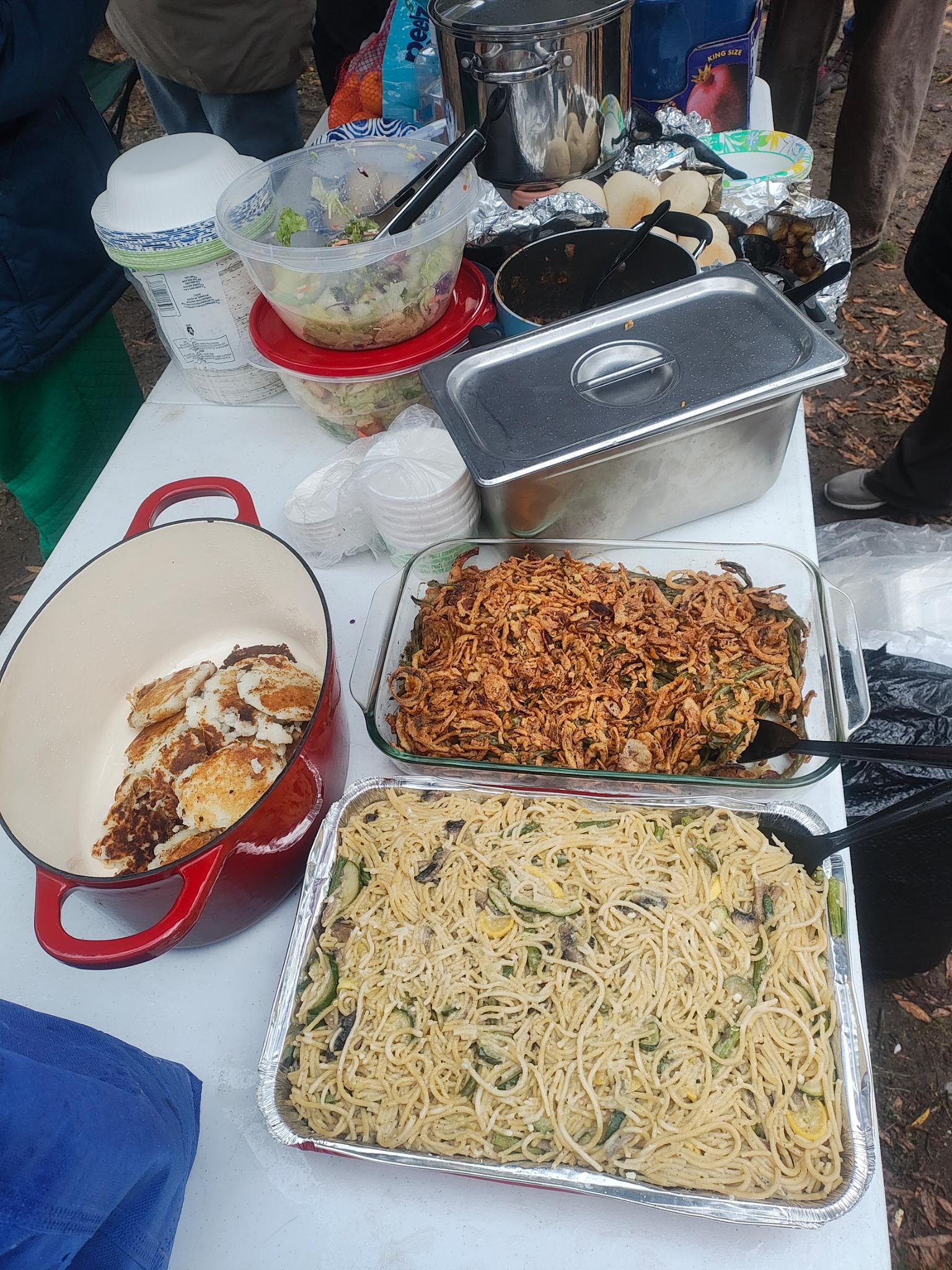 a spread of food on a white table, with green bean casserole, noodles, and pancakes in frame.