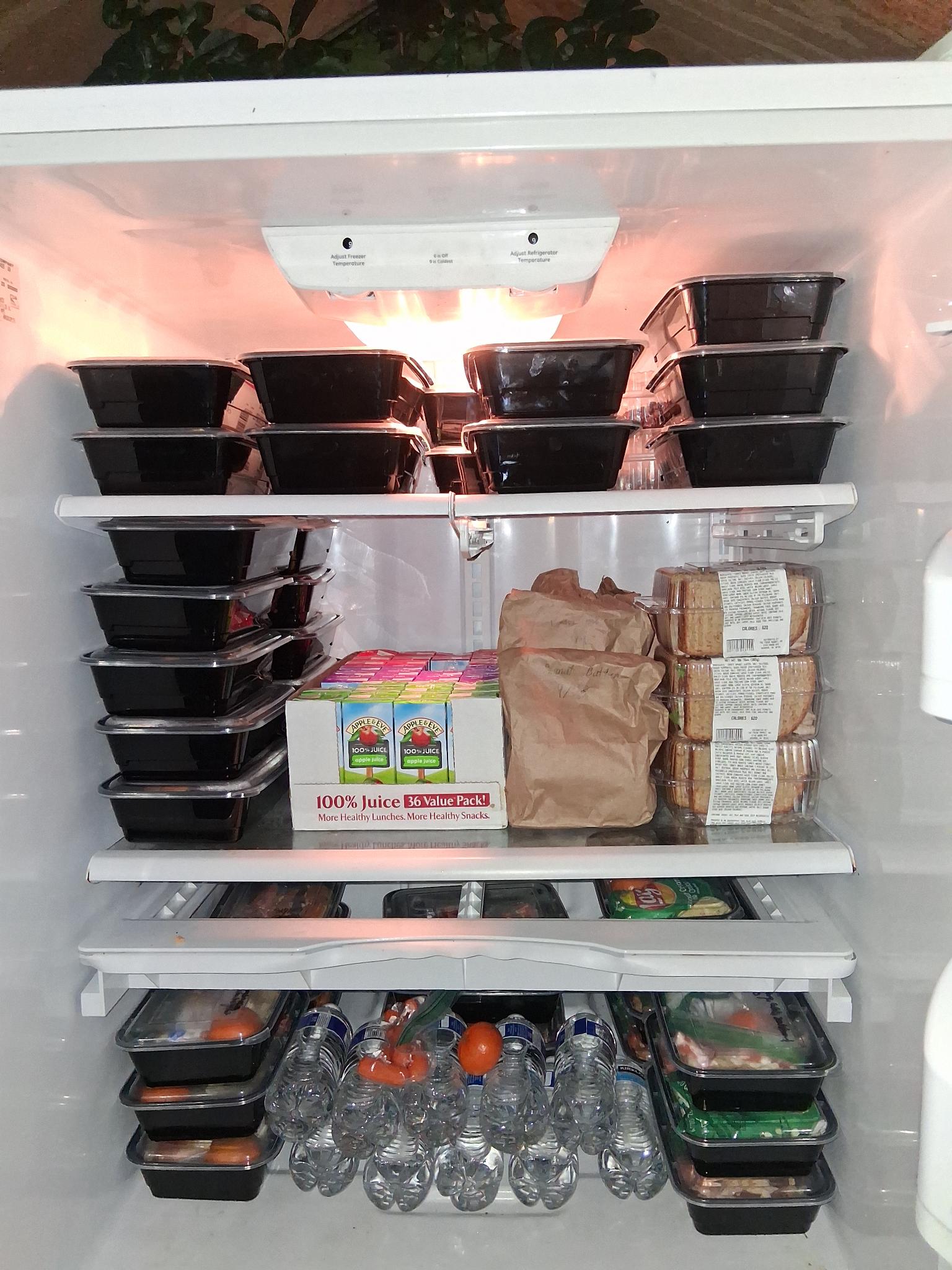 a fridge full of black plastic containers of food and plastic water bottles